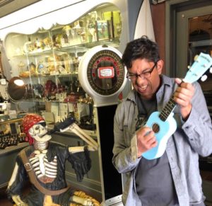 Greg with a blue ukulele and a pirate replica skeleton drinking booze
